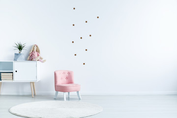 Star stickers on white wall with copy space in child's room interior with pink chair. Real photo