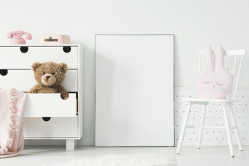 Mockup of empty poster between cabinet with teddy bear and white chair in kid's interior. Real photo. Paste your poster here © Photographee.eu