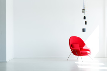 Copy space on white empty wall in minimal living room interior with red armchair under lamp. Real...