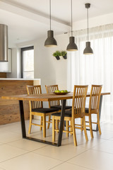 Lamps above wooden table and chairs in minimal bright dining room interior. Real photo