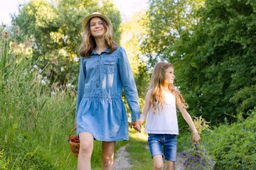 Fototapeta premium Children girls on forest road holding hands. Sunny summer day, girl holding basket with berries