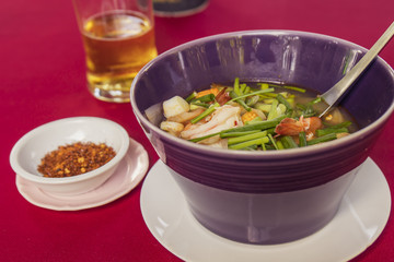 Traditional Thai kitchen tom-yum soup served with grounded chilli peppers and bear on intense red background