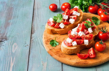 Italian bruschetta with tomato and cheese on toasted toast, blue wooden background. Copy space, selective focus.