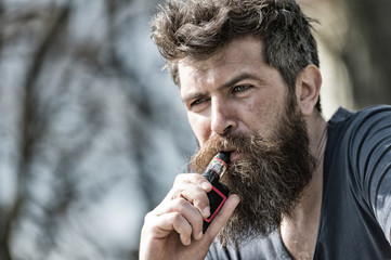 Bearded man smokes vape close up. Electronic cigarette concept. Man with long beard and clouds of...