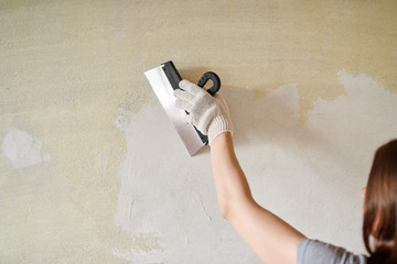 Woman plastering the walls with finishing putty in the room.