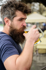 Man with beard and mustache holds glass with beer while relaxing at cafe terrace. Guy having rest with cold draught beer. Hipster on calm face drinking beer outdoor. Draught beer concept.