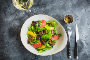 Tasty fresh salad with citrus, lettuce and chicken liver in a plate and glass of vine. Flat lay, top view 