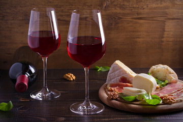Glasses of wine with cheese, bread, nuts, prosciutto and basil. Wine and food on wooden table. horizontal, room for text