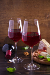 Glasses of wine with cheese, bread, nuts, prosciutto and basil. Wine and food on wooden table. vertical, room for text