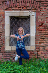 Attractive blond mature woman doing yoga poses outdoor, in front of old fortress, forming the heart with her fingers. Longevity concept 