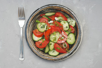 Tomato and cucumber salad with black pepper vegan food with fork gray textured cement background