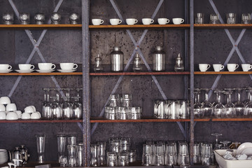 Glasses and coffee cup arranged on a dark raw metal made shelves in urban coffee bar