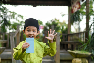 A Malay boy in Malay traditional cloth showing his happy reaction after received money pocket during Eid Fitri or Hari Raya celebration.