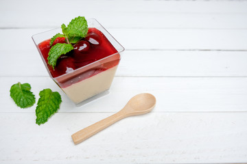 Panna Cotta Strawberry in a glass Placed on a white table. There is a wooden spoon on the side. And...