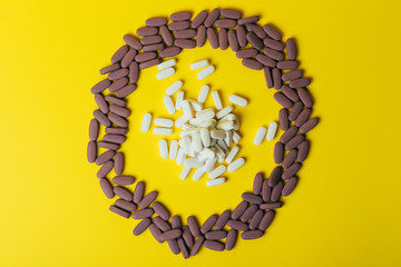 a lot of violet, oval tablets, pills scattered, scattered on a yellow background in the form of a circle, in the middle of the circle are scattered white pills, oval, space for text