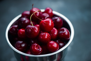 Cherries with a small metal bucket on a grey concrete background, summer berries concept with copy space. Neutral color tones still life
