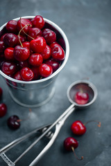 Cherries with an ice cream spoon and metal bucket on a grey concrete background, Summer berries concept with copy space. Neutral color tones still life