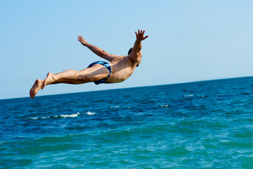 Sporty healthy man jumping into the sea during summer vacation