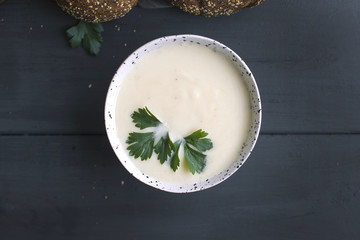 Cream of cauliflower soup with cream and greens, in a white cup on a wooden board and black...