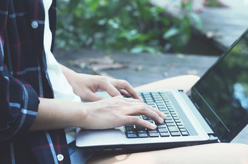 beautiful asian woman hands using laptop typing keyboard for working or searching web browser internet online in social network for some data at outdoor in the park.