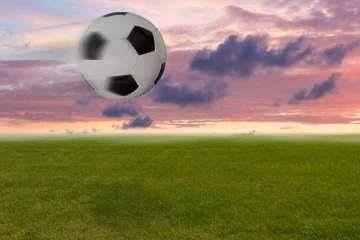 Papier Peint photo Foot Fliegender Fußball vor rotem Himmel am Abend