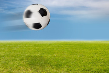 Fliegender Fußball über dem Rasen vor blauem Himmel