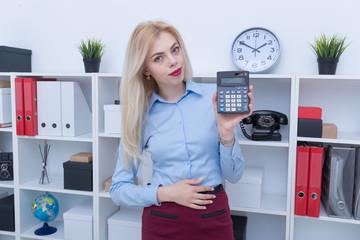 Portrait of a girl in a blue shirt and skirt counts on a calculator in the office