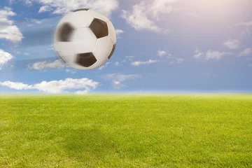Papier Peint photo Foot Fliegender Fußball über dem Rasen vor blauem Himmel
