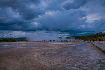 Outdoor view of tourists walking on a boardwalk in the horizont, around the Grand Prismatic Spring in Yellowstone National park, this geyser is one of the most active