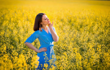 Naklejka na ściany i meble Allergy free concept. Freedom. Attractive girl in blue dress on yellow blooming meadow. Summer sunny portrait of brunette girl.