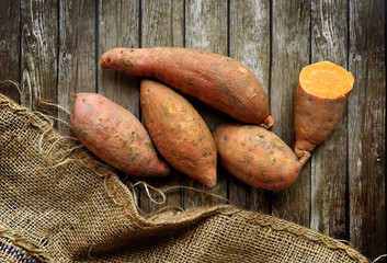 sweet potatoes over wooden background with rustic sack