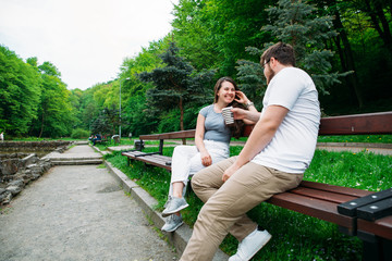 couple sitting on bench. talking and drinking coffee in park