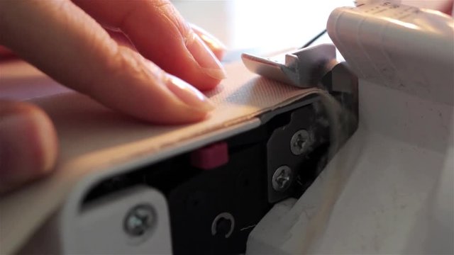 A woman working on a sewing project as she cuts fabric and sews it on a machine. sewing machine close up A hand of a dressmaker supporting a cloth while sewing on a machine.