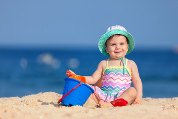 Happy childhood, happy family vacation. Cute child on the sea background. Happy little girl playing with sand on the beach of sea. Summer vacation. Summer lifestyle