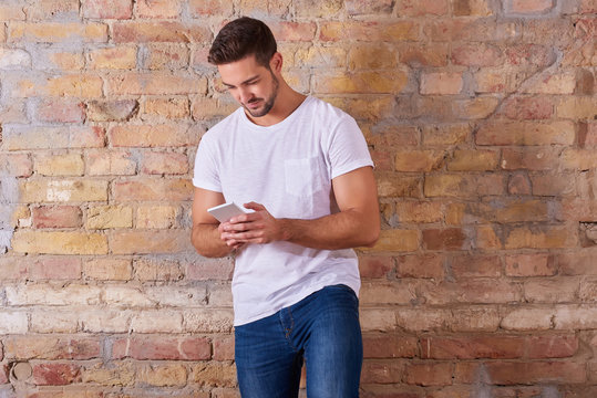 A serious handsome young man using his smartphone in a white tshirt.