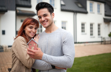 Young smiling couple standing outside their new house, family and real estate concept