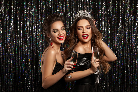Two beautiful young girls smiling and holding a glass of champagne, meeting Christmas and New Year. Clean skin and a hairstyle with bright lips. Photographed on a sparkling background.