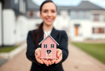 Real estate agent with model of house in front of home for sale
