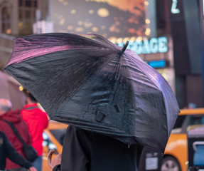 Man holds black umbrella with reflection of neon advertisement in Times Square, New York City