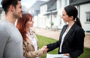 Real estate agent shaking hands with customers after buying new house in residential area