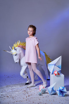 Romantic little girl in elegance dress pink color. Fashion lady teenage girl with make-up poses for children's clothing catalog,studio. Designer collection. White big unicorn origami made of paper.