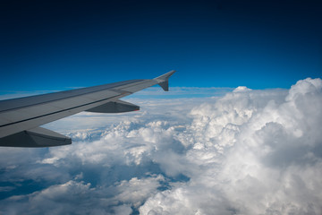 Beautiful view of the airplane wing and white loose clouds in the blue sky from the window of the plane.