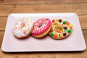 Three appetizing donuts lie on a pink ceramic plate.