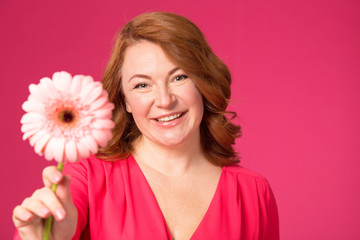 Beautiful happy woman with gerbera flower in hands on a pink background.