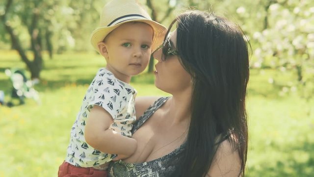 Young mother with her adorable two year old boy playing outdoors with love in slow motion. Mother kisses little son looking at camera. Concept of happy family love