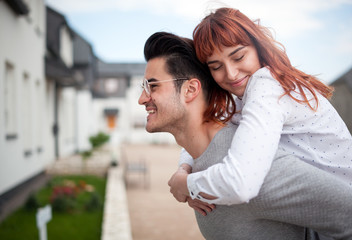 Man carrying wife on his back in front of their new home, happy couple after buying real estate