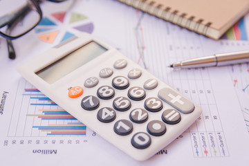 data analyzing with calculator, notebook and pen. on charts and graph to find out the result.