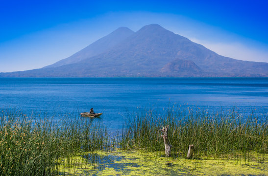 Outdoor view of totora acuatic plants in the border of the lake, with unidentified fisherman in a small boats in Atitlan Lake, with San Pedro volcano in Background