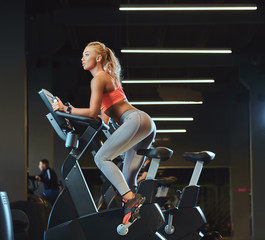 Young beautiful blonde woman in sportswear training on an exercise bike in modern fitness center.