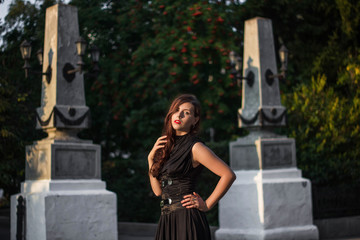 Young, beautiful girl in a black dress with a corset, on a park background and stone columns with lanterns.